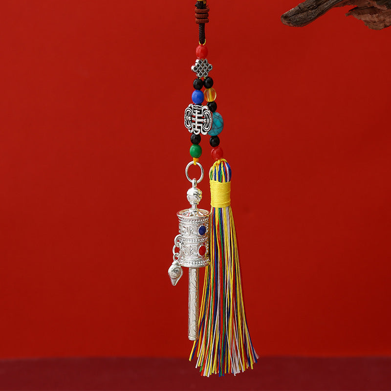Tibetan Prayer Wheel Keychain – silver-tone prayer wheel pendant with colorful silk tassel, turquoise beads and full braided cord, red background, front vertical view