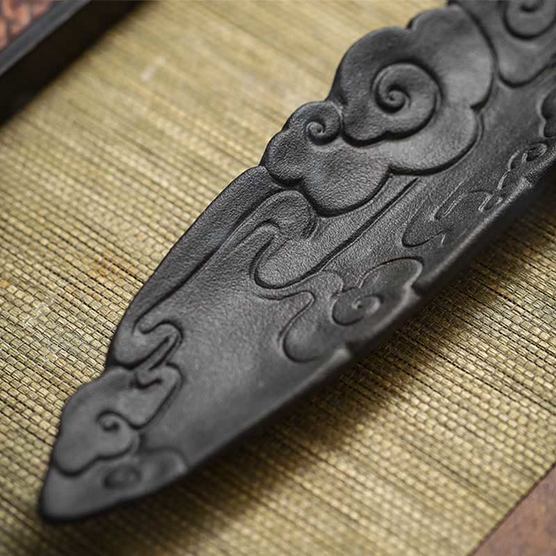 Macro detail of ruyi cloud carvings on dark ceramic incense holder, woven bamboo mat, diagonal close-up – Pixiu incense burner texture