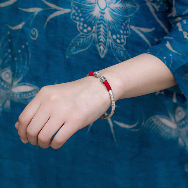 Tibetan Red String Bracelet – worn on wrist over blue floral batik fabric, silver engraved bangle