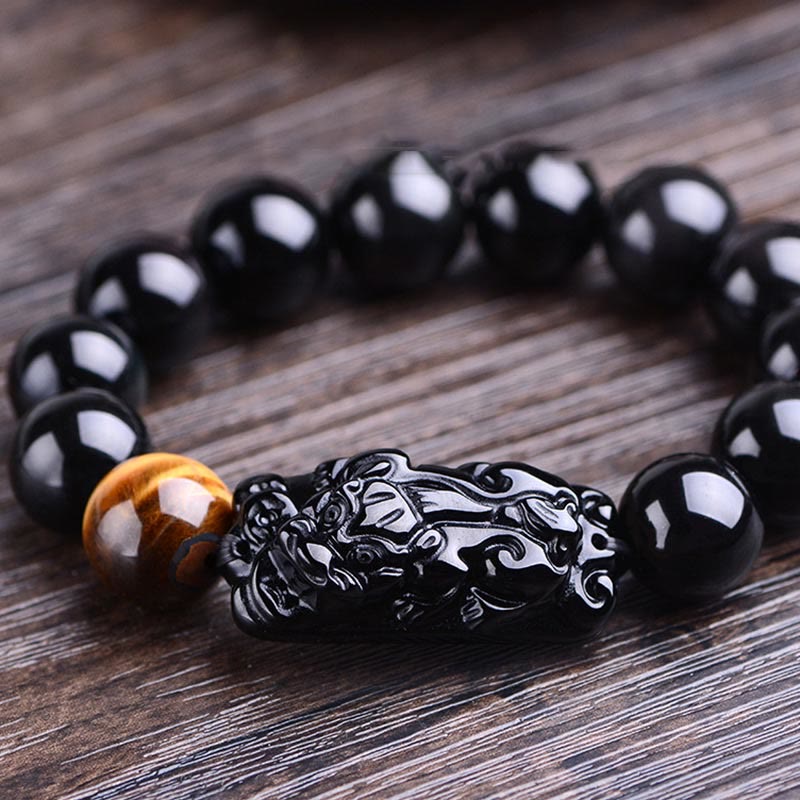 Black Obsidian PiXiu Tiger Eye Bracelet low angle on aged wood, carved creature detail, glossy polished beads