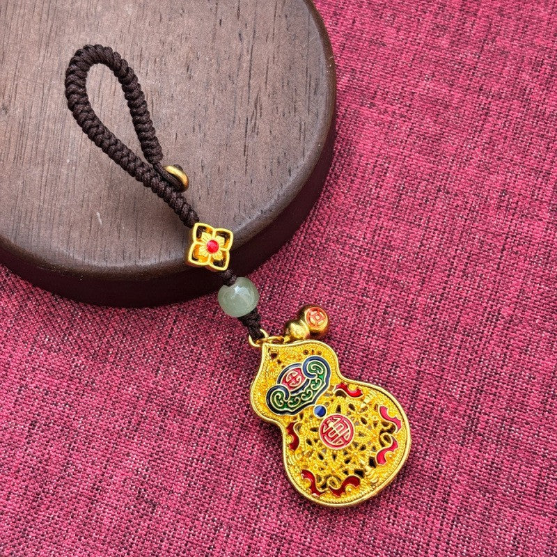 Gold enamel calabash keychain with jade bead and small gourd charm, brown cord on pink fabric