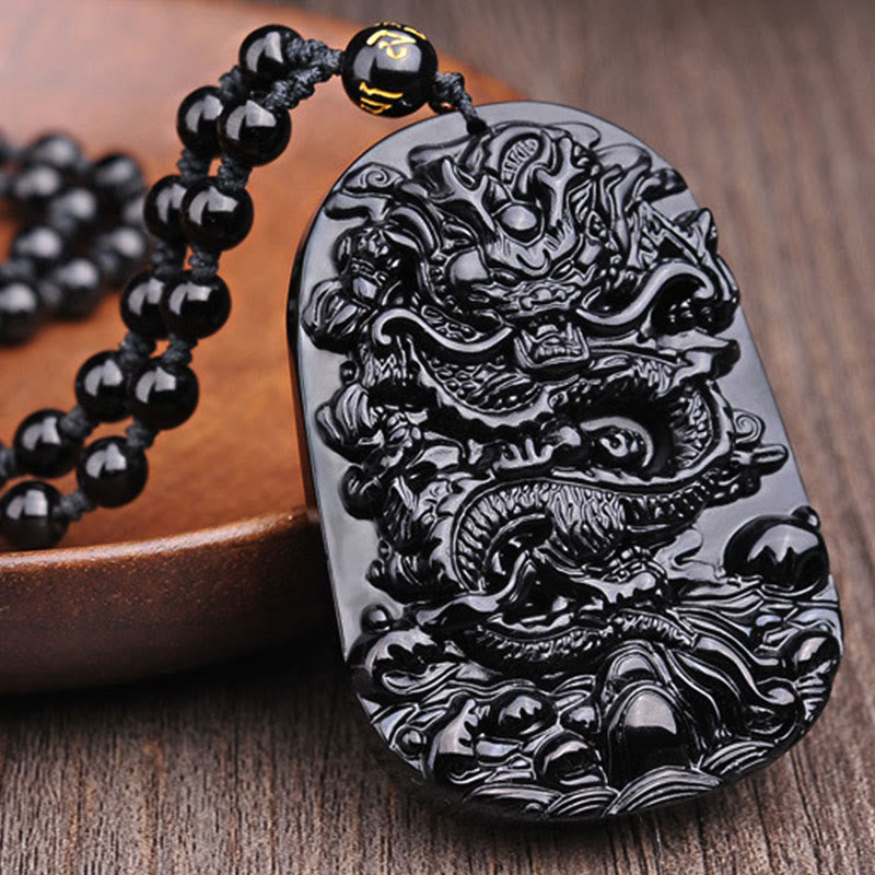 Black Obsidian Dragon Pendant – Three-quarter dragon plaque on wood grain with ceramic vessel, artisan