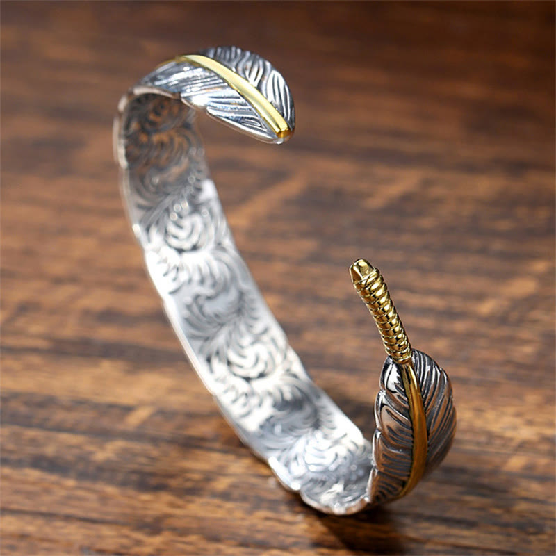 Two-tone feather cuff bracelet with silver body, gold spine accents, carved feather vein texture and engraved interior scrollwork on wood