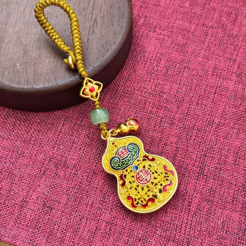 Gold enamel calabash keychain with jade bead and small gourd charm, gold cord on pink fabric
