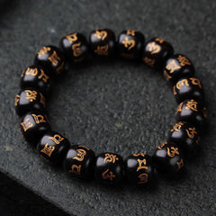 Ebony Wood Om Mani Padme Hum Bracelet – Circular arrangement on dark stone showing gold inscriptions, prayer beads