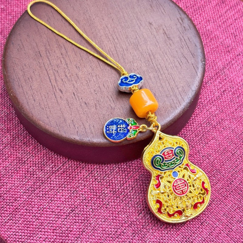 Gold enamel calabash keychain with jade bead and small gourd charm, yellow cord on pink fabric