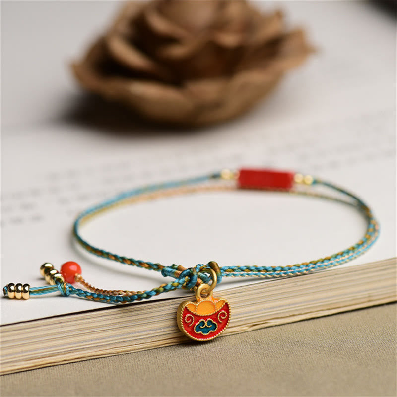 Cinnabar Bracelet - Gold ingot charm on braided cord resting on open book, auspicious jewelry
