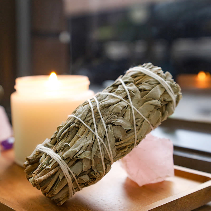 White sage smudge stick with rose quartz crystal and candle on wooden tray