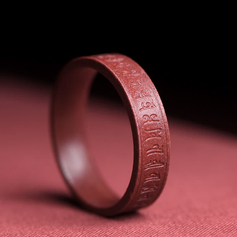 Cinnabar Om Mani Padme Hum Blessing Ring – matte cinnabar band with engraved Sanskrit mantra script, dark gradient background