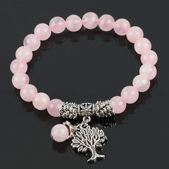 Tree of Life rose quartz bracelet with pink translucent beads, ornate silver floral spacer, detailed tree pendant with roots and foliage on black background.