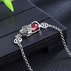 Copper Garnet PiXiu Wealth Bracelet – Close-up of red garnet PiXiu with silver coin links on black wood