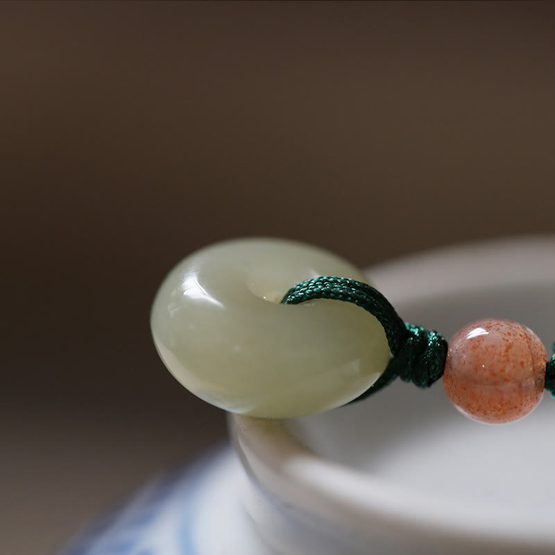 Jade Peace Buckle Lotus Necklace – Macro close-up of celadon jade bi-disc with pink bead on green cord, jade pendant