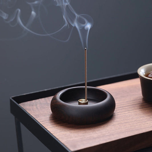 Dark wood incense bowl with brass insert and rising smoke, mindful