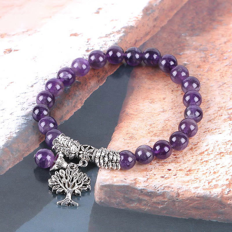 Tree of Life amethyst bracelet with purple gemstone beads, silver tree pendant with intricate branches, silver floral spacers on weathered stone.