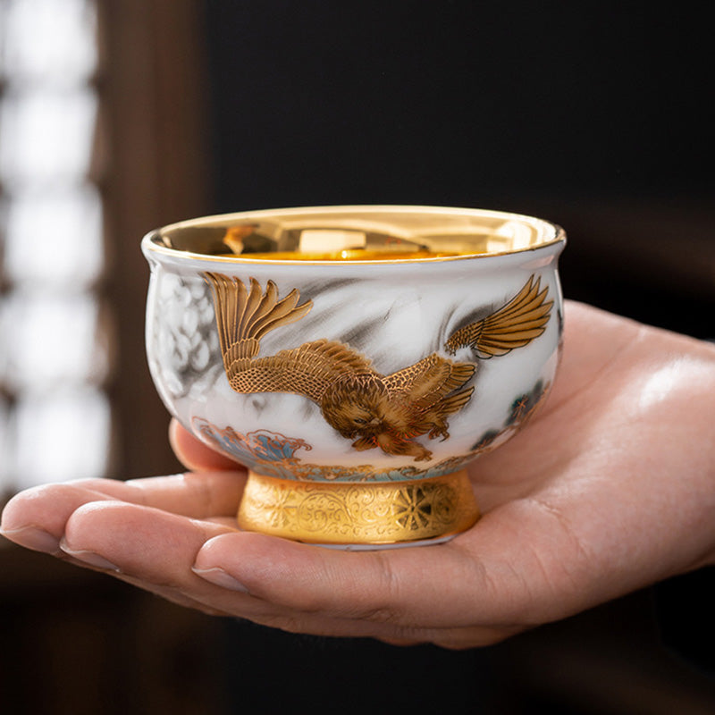 Golden Eagle Dragon Gilt Ceramic Teacup – sculptural golden eagle relief on marbled white porcelain, gold interior, held in palm
