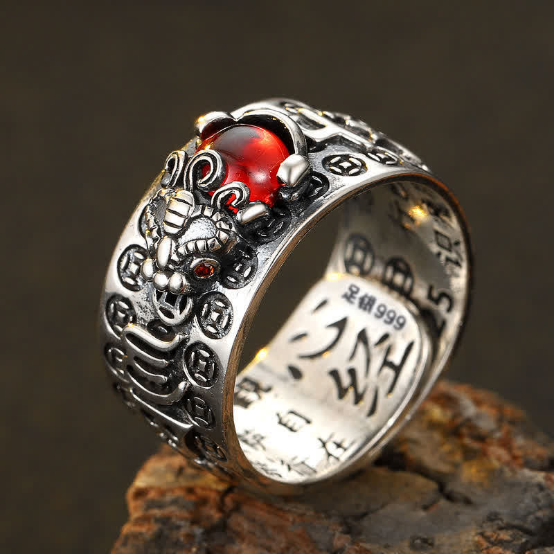PiXiu Garnet Heart Sutra Ring – Silver ring with lion head design and red gemstone on rough brown stone against dark gradient background, side profile view