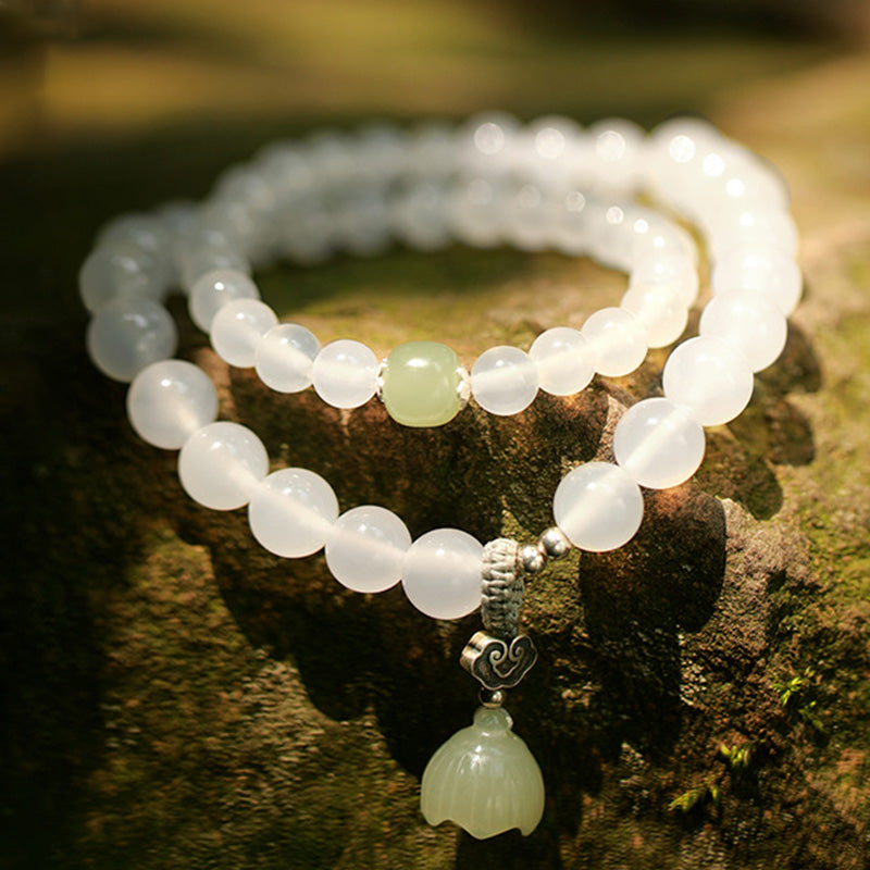 White Agate Jade Lotus Bracelet - Lotus flower pendant with silver yin-yang charm on mossy wood, warm sunlight, zen jewelry