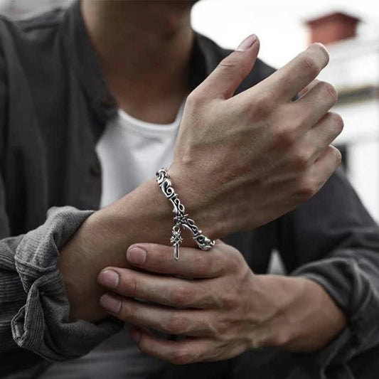 Men's oxidized silver Viking twisted cuff bracelet with Celtic knotwork pattern and dangling cross charm worn with gray jacket showing adjustable open cuff design