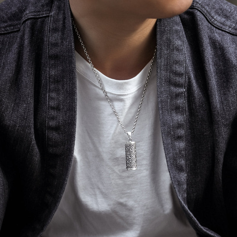 Om Mani Padme Hum Silver Protection Necklace – Oxidized silver cylindrical pendant necklace with swirling cloud pattern on cable chain, worn with white t-shirt under dark denim jacket