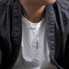 Om Mani Padme Hum Silver Protection Necklace – Oxidized silver cylindrical pendant necklace with swirling cloud pattern on cable chain, worn with white t-shirt under dark denim jacket