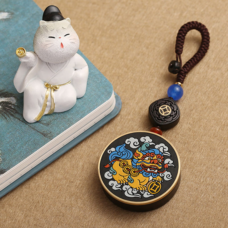 PiXiu Coin Keychain – Laying near white lucky cat figurine on blue book