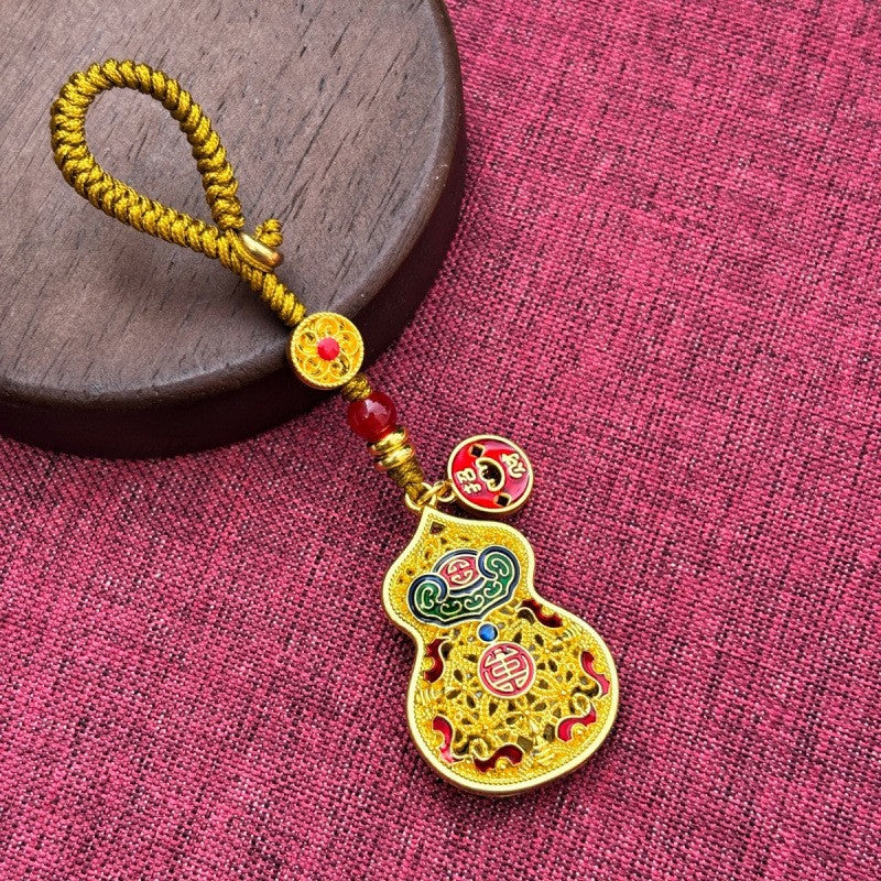 Hand holding gold rotating calabash disc keychain with longevity charm by car key, outdoor