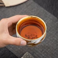Golden Eagle Dragon Gilt Ceramic Teacup – gold dragon motif exterior with reflective gold interior, amber tea in hand, artisan