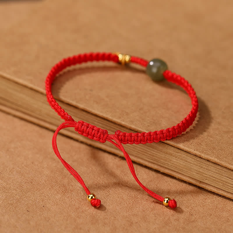 Adjustable red cord bracelet with green Hetian jade bead gold-toned fu blessing charm and gold end caps shown in flat lay on pure white background for e-commerce catalog