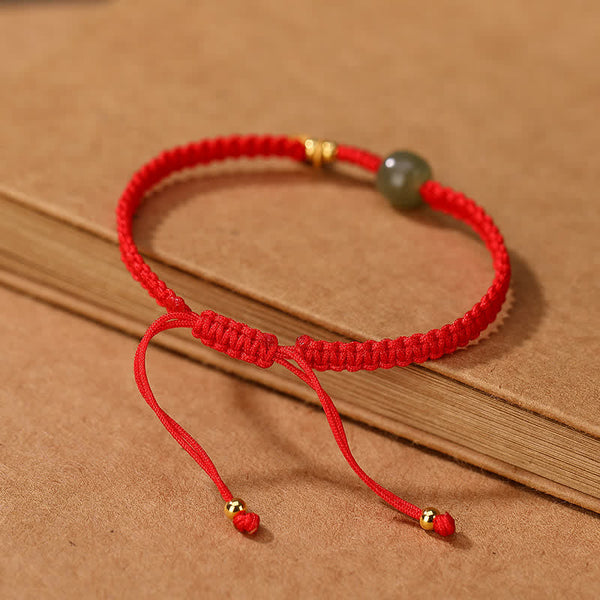 Adjustable red cord bracelet with green Hetian jade bead gold-toned fu blessing charm and gold end caps shown in flat lay on pure white background for e-commerce catalog