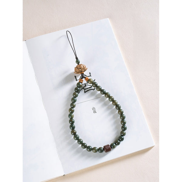 Zodiac Wood Bead Lanyard – Green sandalwood lotus lanyard placed on white book with Chinese characters, artistic product flat lay