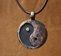 Yin Yang Pendant – aged bronze yin-yang medallion front view with braided cord, earth tone backdrop