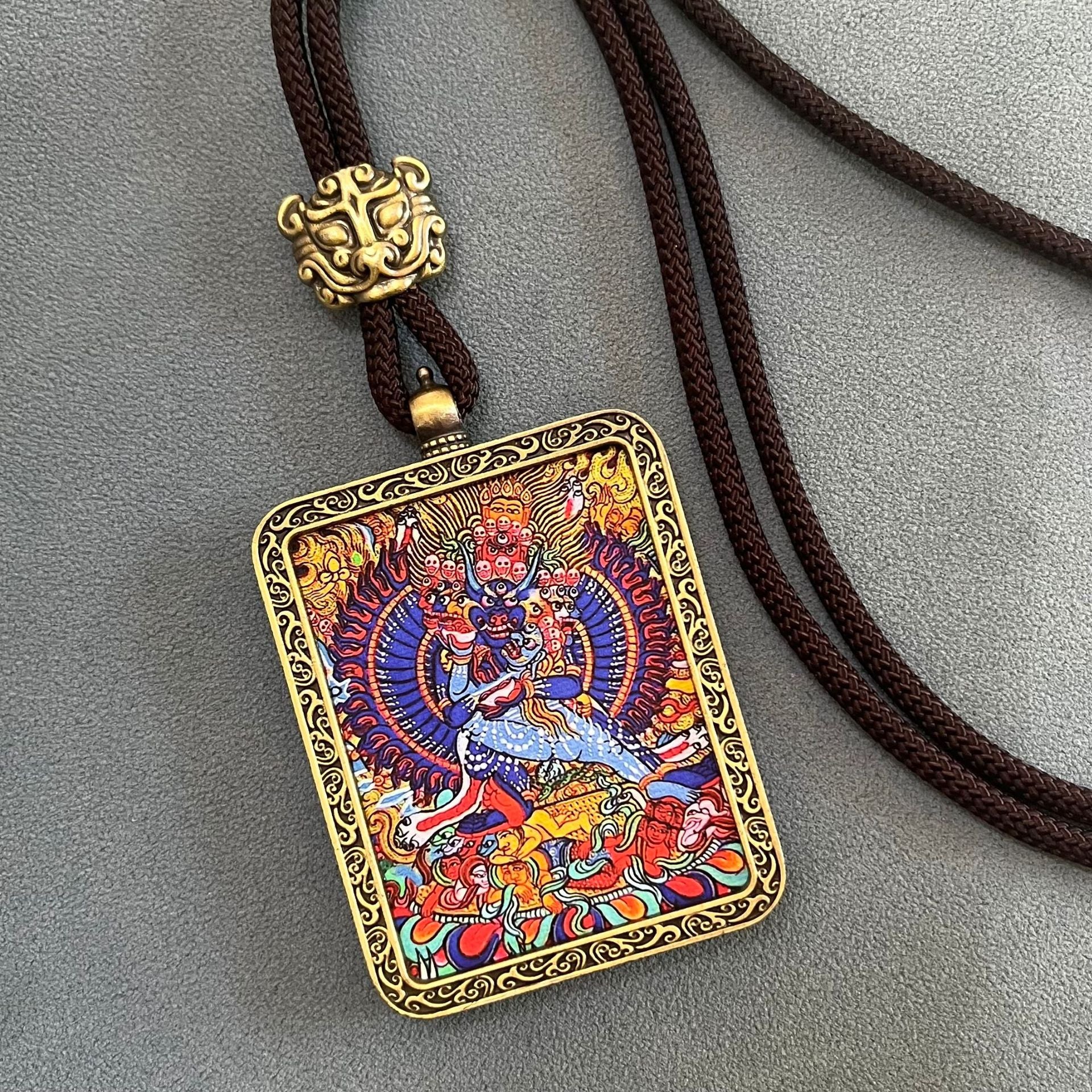 Tibetan Thangka Pendant – multi-headed blue deity on mythical animal, gold border, brown rope with beast clasp, sacred art