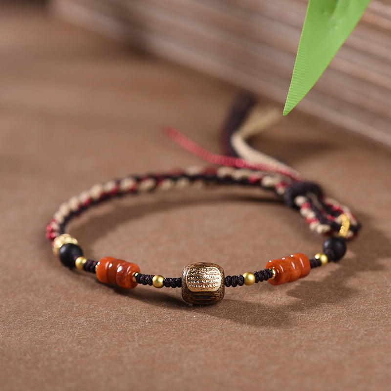 Woven Bracelet – close-up gold etched barrel bead with orange agate wheels and black beads on brown surface, boho chic