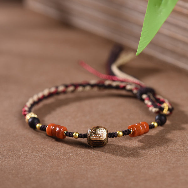 Woven Bracelet – close-up gold etched barrel bead with orange agate wheels and black beads on brown surface, boho chic