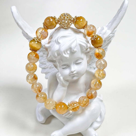 Natural Citrine Bracelet – golden yellow and clear citrine beads with gold filigree spacer beads, draped over white angel figurine wings, clean white background, artistic product display
