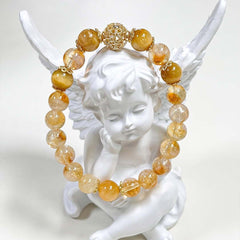 Natural Citrine Bracelet – golden yellow and clear citrine beads with gold filigree spacer beads, draped over white angel figurine wings, clean white background, artistic product display