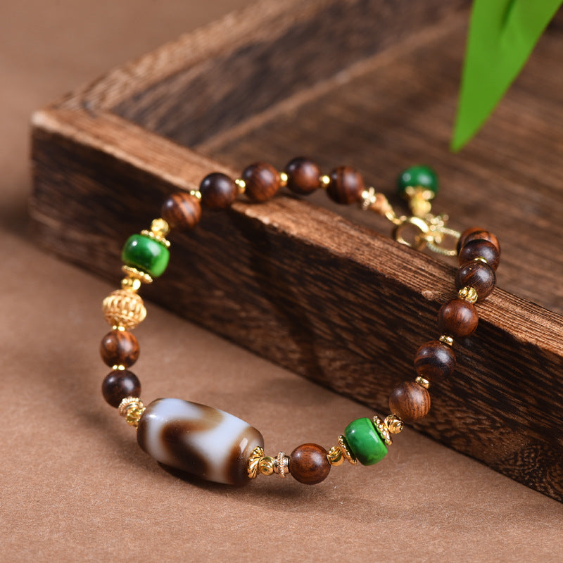 Dzi Rosewood Bracelet – Rosewood and dzi bead bracelet draped on dark wood block with green leaf, zen jewelry