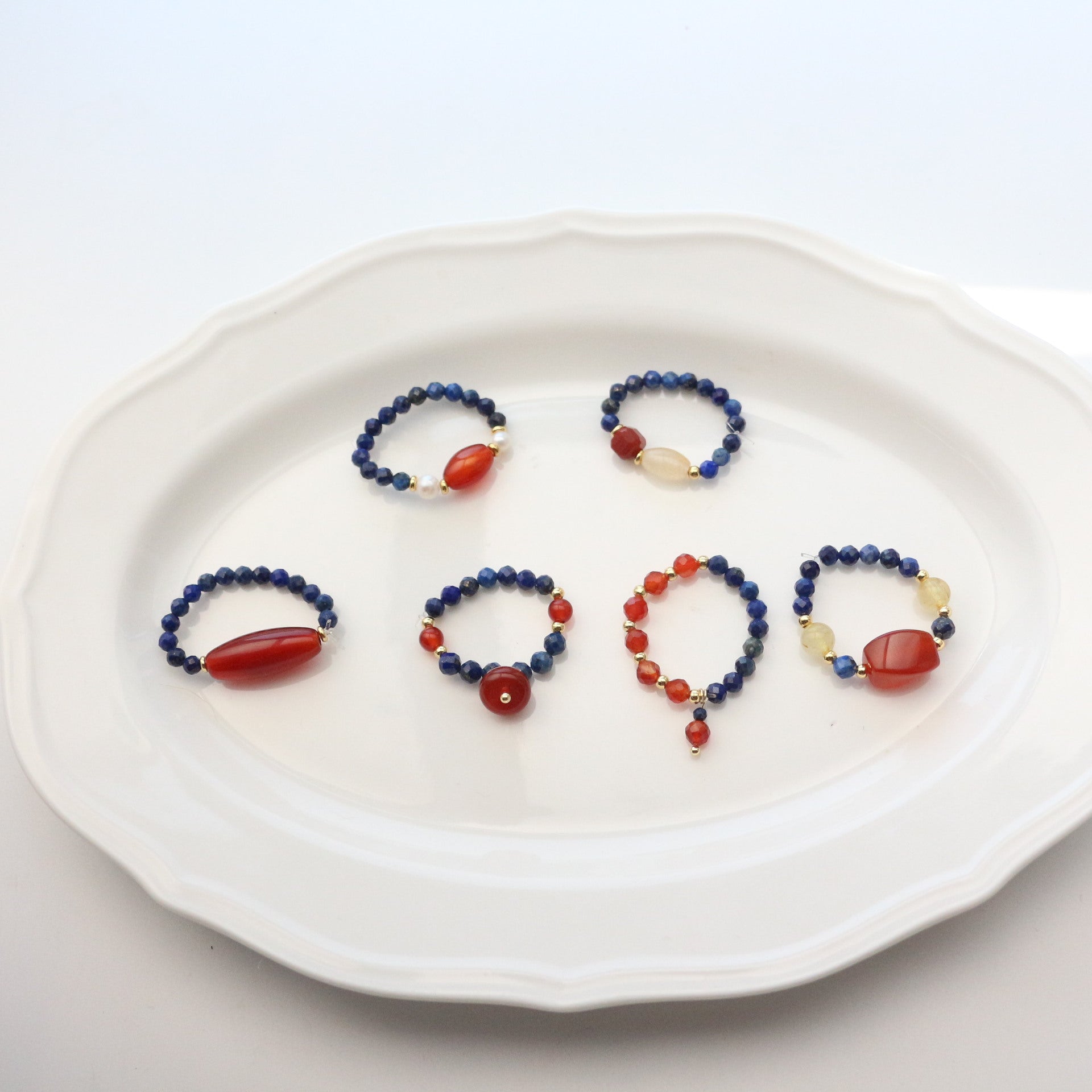 Lapis Lazuli Agate Ring Set – six rings arranged on white scalloped plate, blue lapis and red agate bead combinations, gemstone ring set