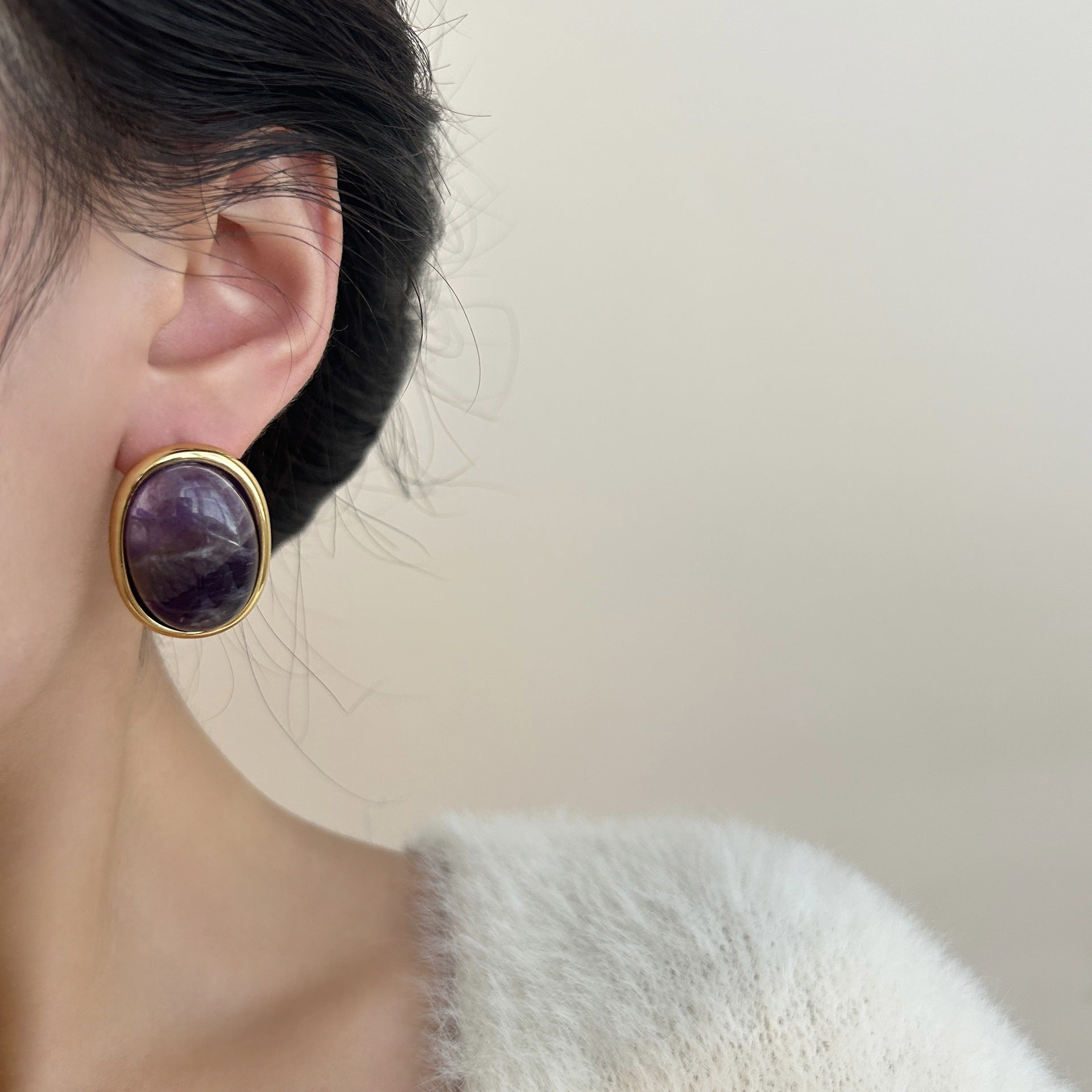 Amethyst Stud Earrings – oval amethyst stud earring on woman ear with black hair bun and white fuzzy sweater, elegant crystal earring