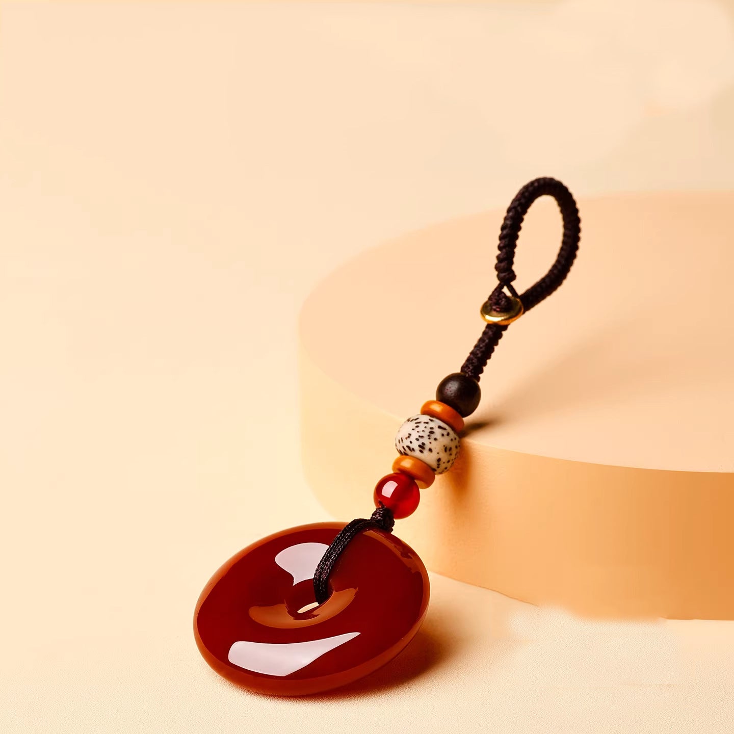 Jade Keychain Pendant – Red-brown jade donut leaning on beige geometric block with bodhi beads, artistic display