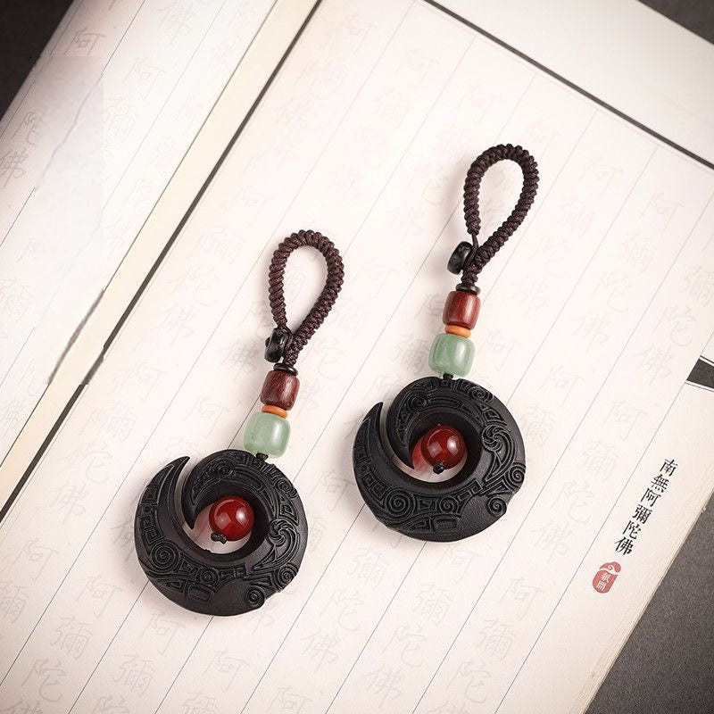 Two Feng Shui ebony wood protection keychains displayed on antique book with Buddhist scripture