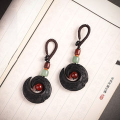 Two Feng Shui ebony wood protection keychains displayed on antique book with Buddhist scripture