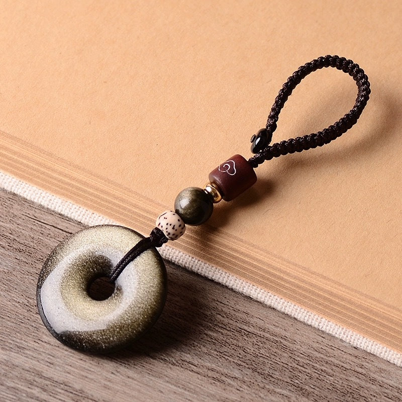 Gold Obsidian Pendant – Gold sheen obsidian keychain with decorative beads on textured beige surface, energy stone