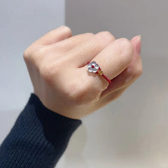 Red String Flower Ring – hand in black sweater sleeve wearing red cord ring, white jade blossom, gold accent, minimalist luck ring