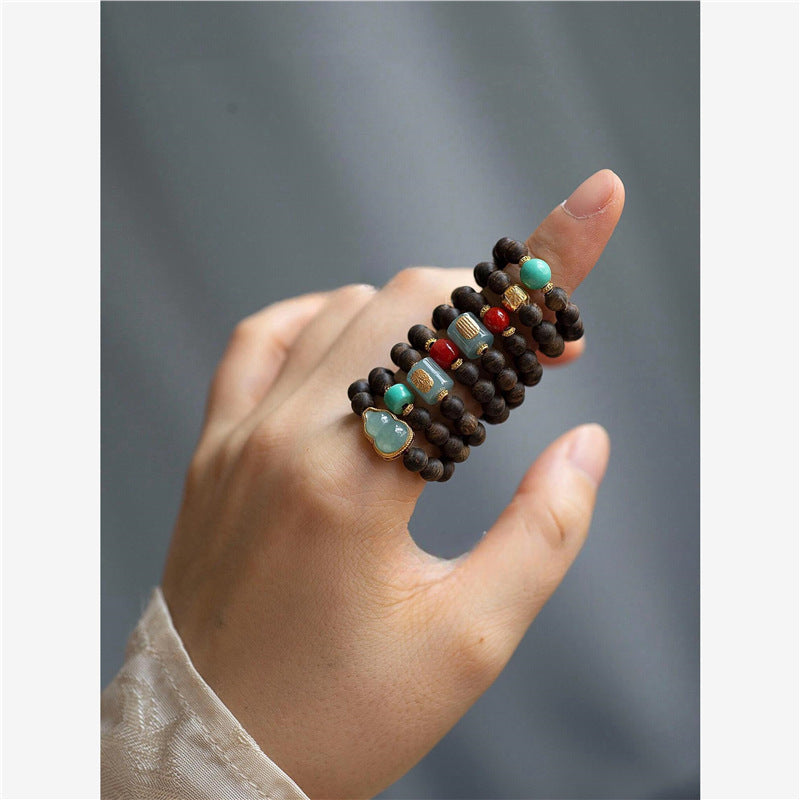 Agarwood Ring – stacked rings with turquoise and red beads on finger, gray textured backdrop