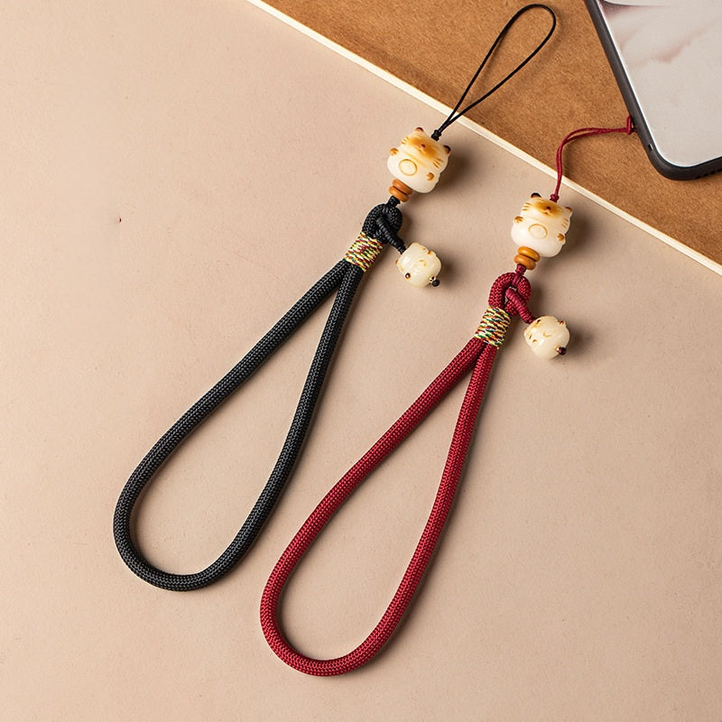 Two Bodhi Maneki Neko phone straps in black and wine red displayed beside a smartphone