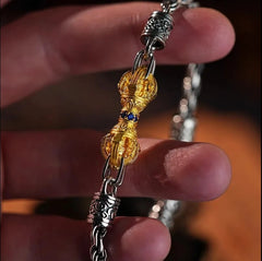 Vajra Bracelet – gold vajra charm held between fingers showing scale and craftsmanship, hand model