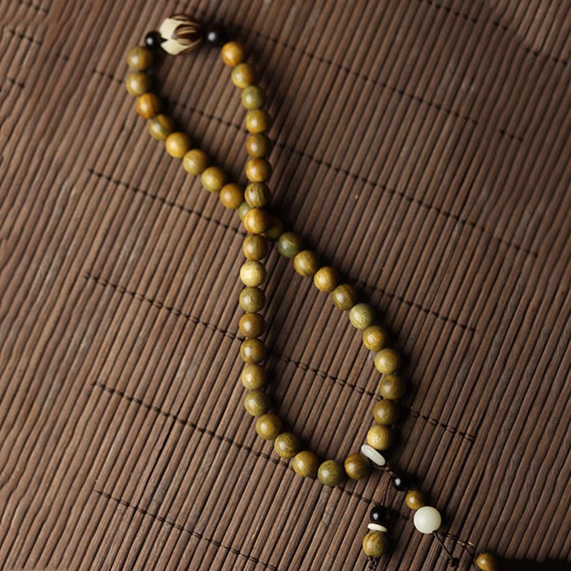 Green Sandalwood Lotus Bracelet – diagonal S-curve on dark bamboo slat mat, full length