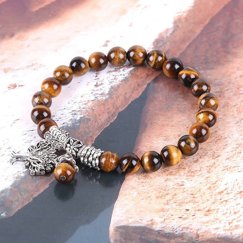 Tree of Life tiger eye bracelet with amber-brown banding beads, silver tree of life pendant, ornate silver barrel spacer on beige fabric.