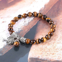 Tree of Life tiger eye bracelet with amber-brown banding beads, silver tree of life pendant, ornate silver barrel spacer on beige fabric.